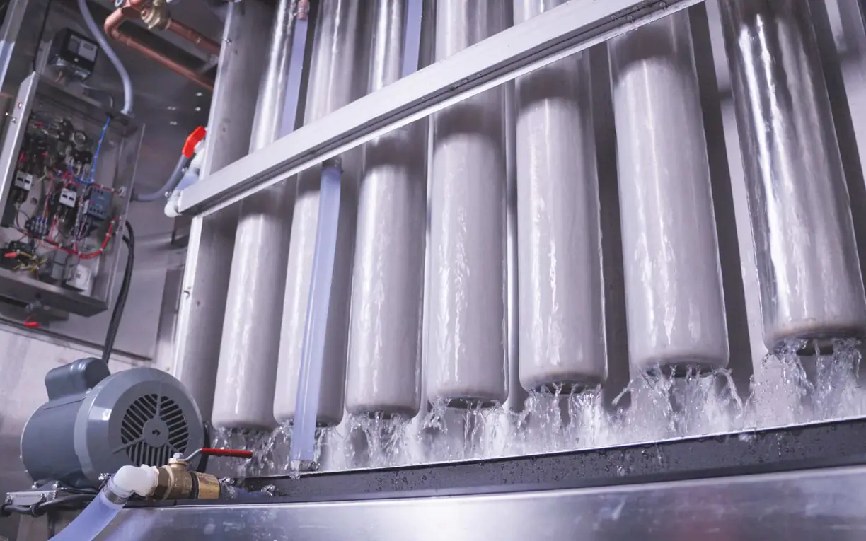 Industrial ice machine manufacturers Evaporator tubes coated in ice with water running down inside an ice machine, with a motor and electrical panel at left