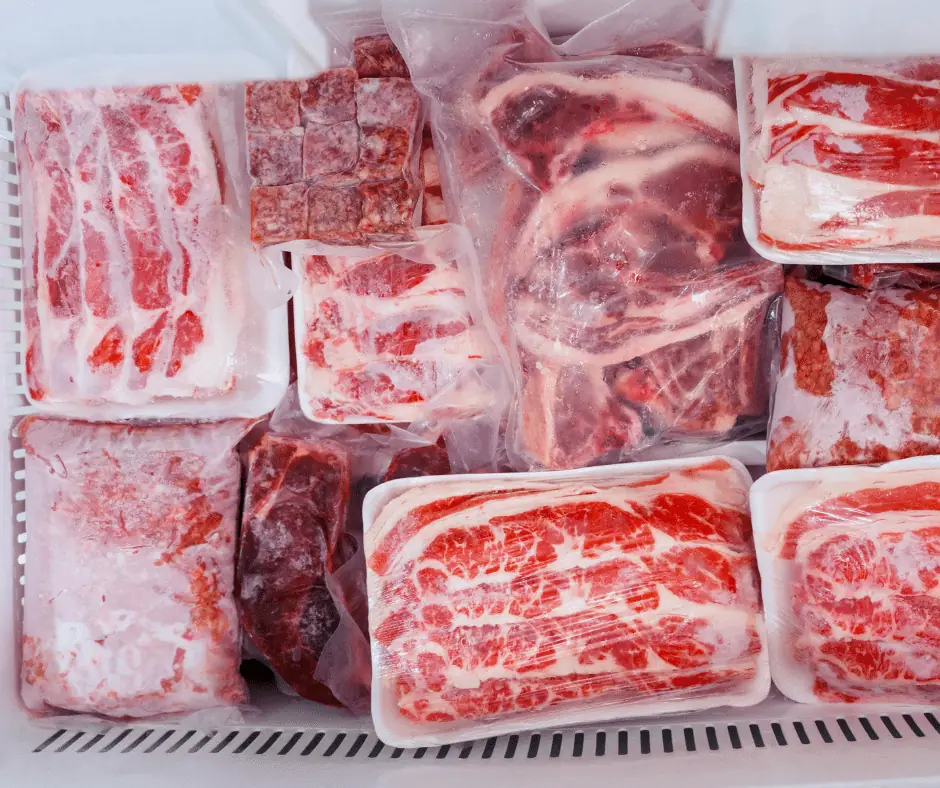 Packages of raw red meat and pork cuts in plastic wrap and foam trays stacked in a freezer