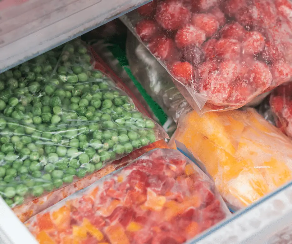Freezer drawer packed with bagged frozen peas, strawberries, mango and diced red peppers