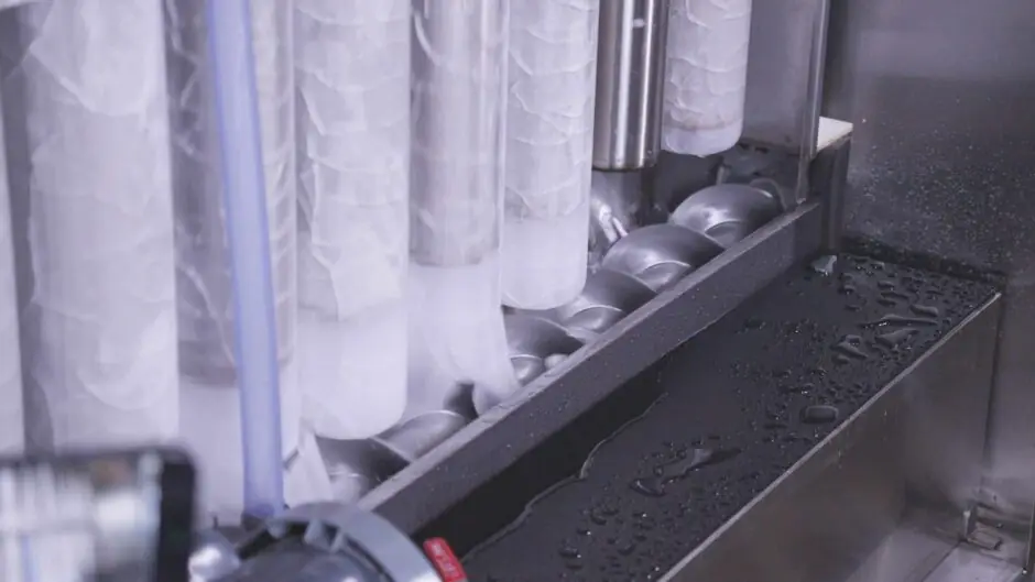Ice-coated evaporator tubes above the cutter screw inside an ice machine, with water droplets on the tray below
