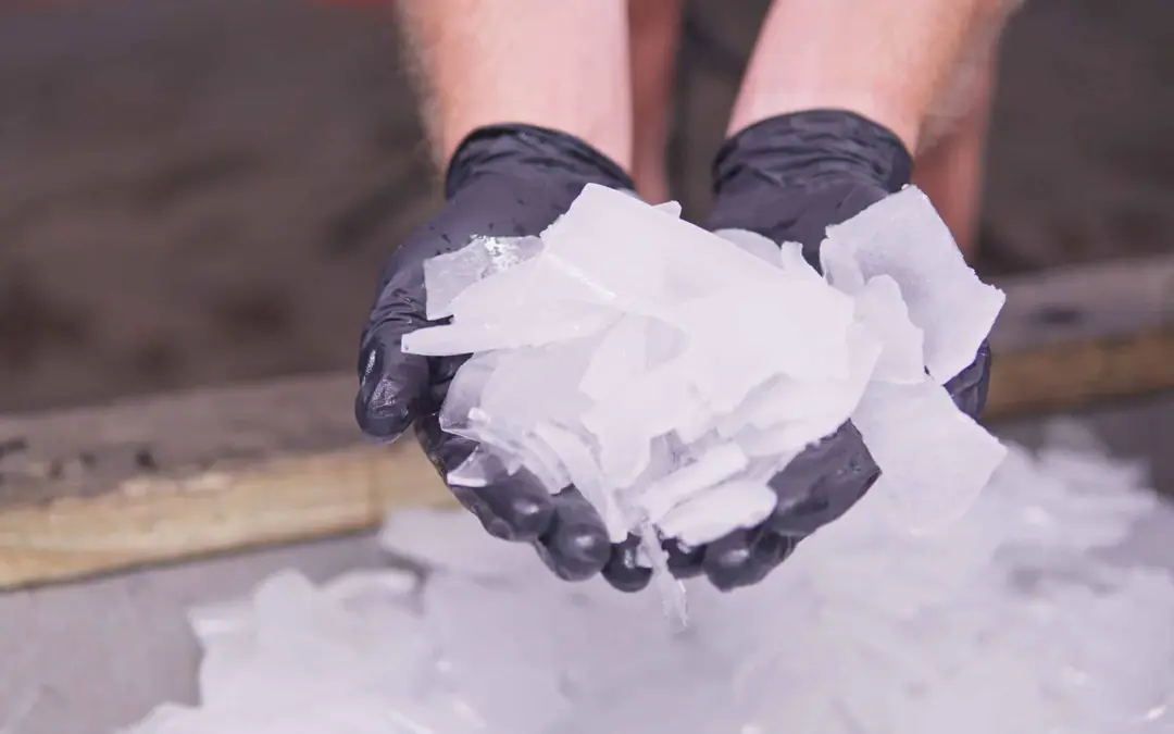 Gloved hands holding fresh hard cracked ice pieces above a larger pile of ice